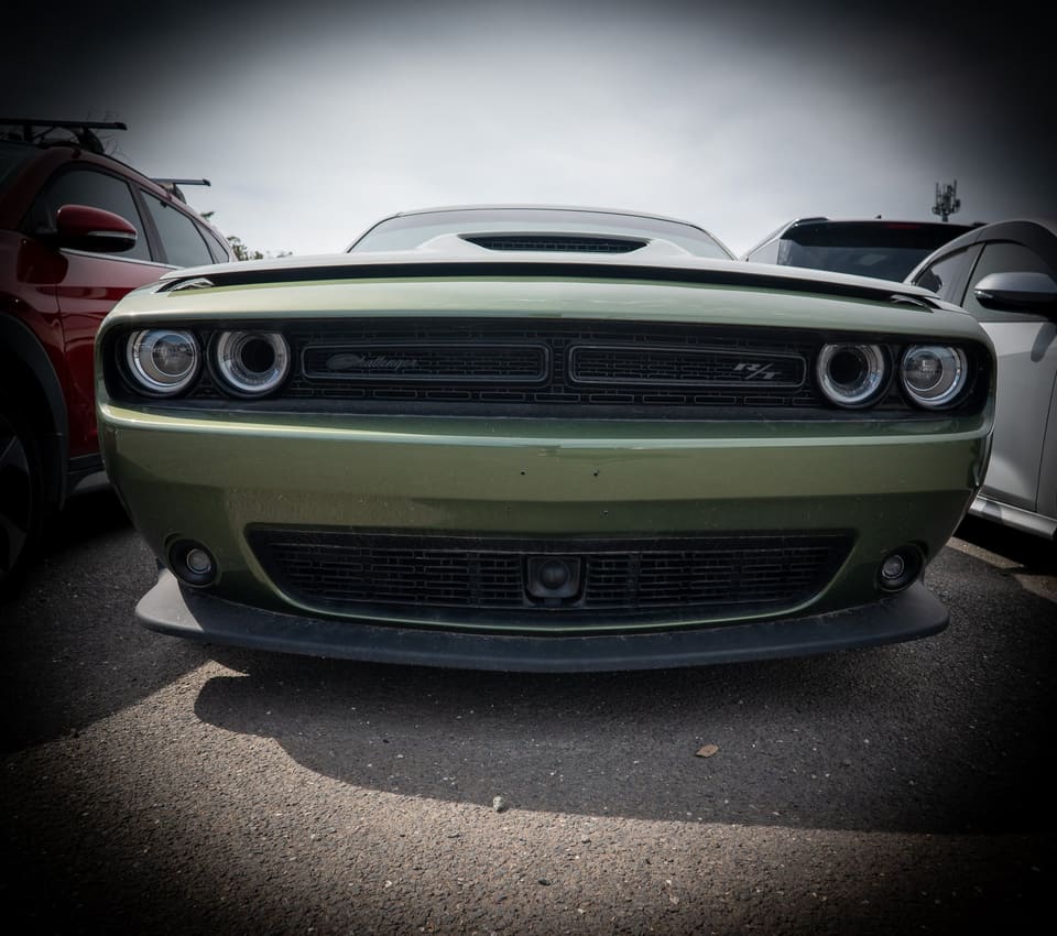 Front-on view of a green Dodge Challenger parked among other vehicles in a storage yard.