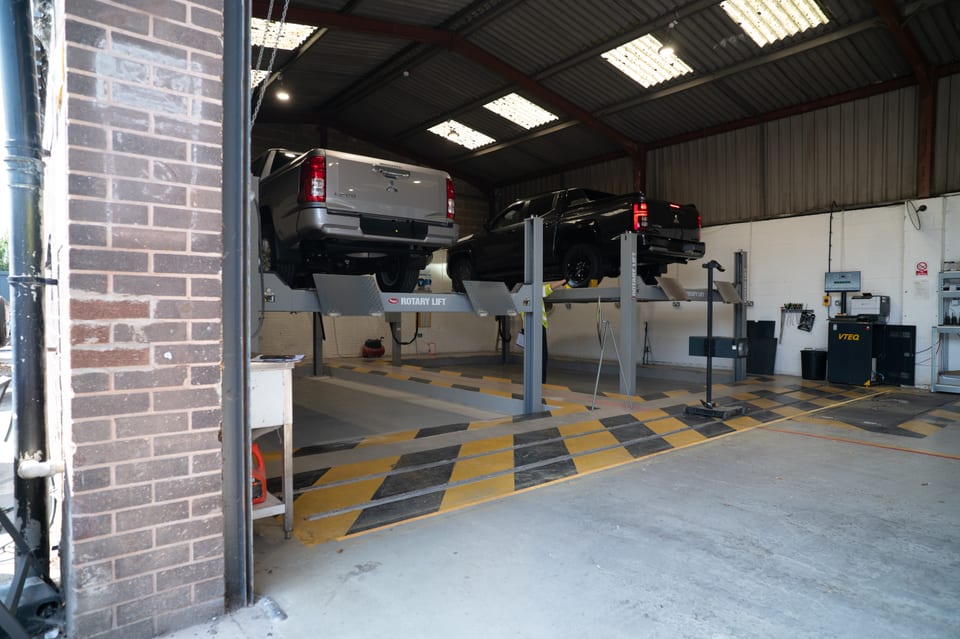 Imported pickups on the four-post lifts in the IVA test lane, raised for underbody checks.