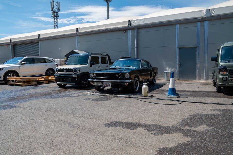 Vehicles including a classic Mustang parked outside a warehouse.