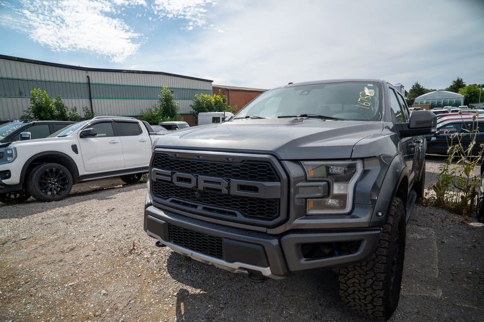 Grey Ford Raptor pickup truck parked in a gravel yard with other vehicles in the background.