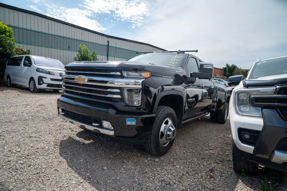 Black Chevrolet Silverado dually pickup truck parked in a yard with a van behind it.