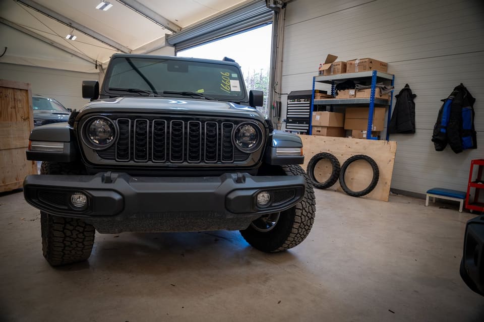 Front view of a grey Jeep Wrangler parked inside a workshop with shelving behind it.